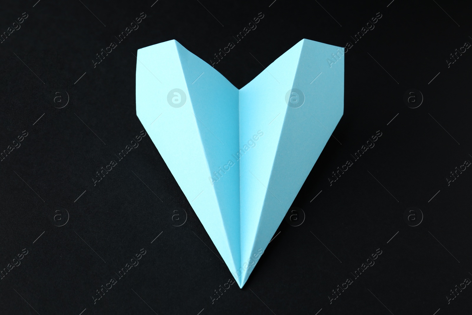 Photo of One handmade light blue paper plane on black background, closeup