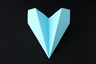 Photo of One handmade light blue paper plane on black background, closeup