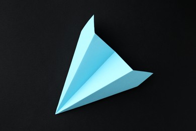 Photo of One handmade light blue paper plane on black background, top view