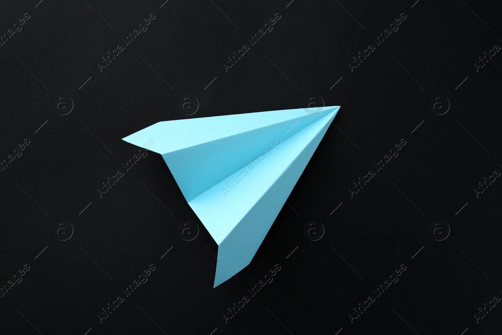 Photo of One handmade light blue paper plane on black background, top view