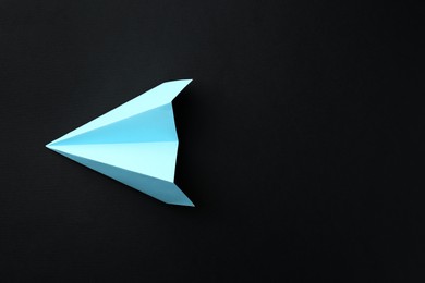 Photo of One handmade light blue paper plane on black background, top view. Space for text