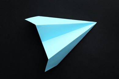 Photo of One handmade light blue paper plane on black background, top view