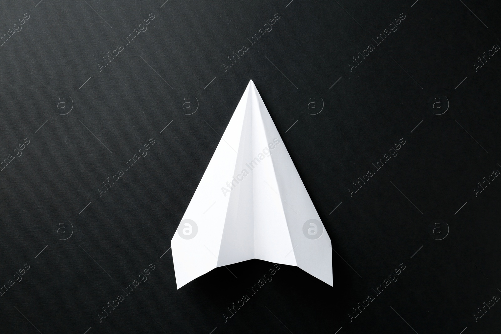 Photo of One handmade paper plane on black background, top view