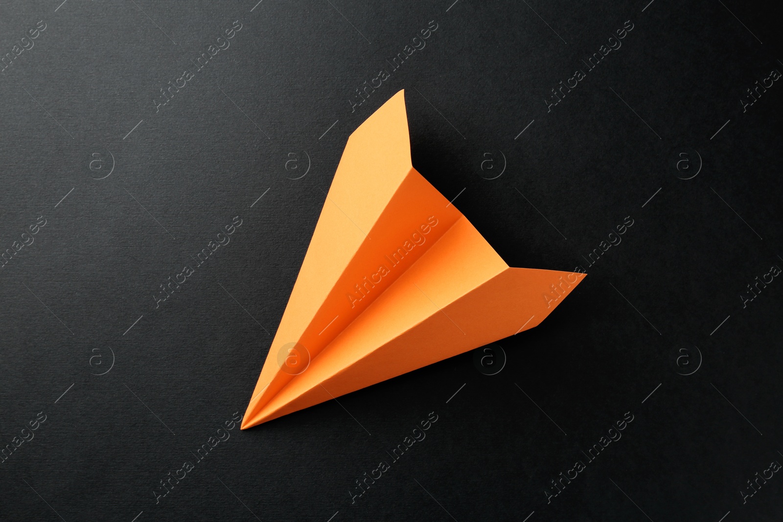 Photo of One handmade orange paper plane on black background, top view