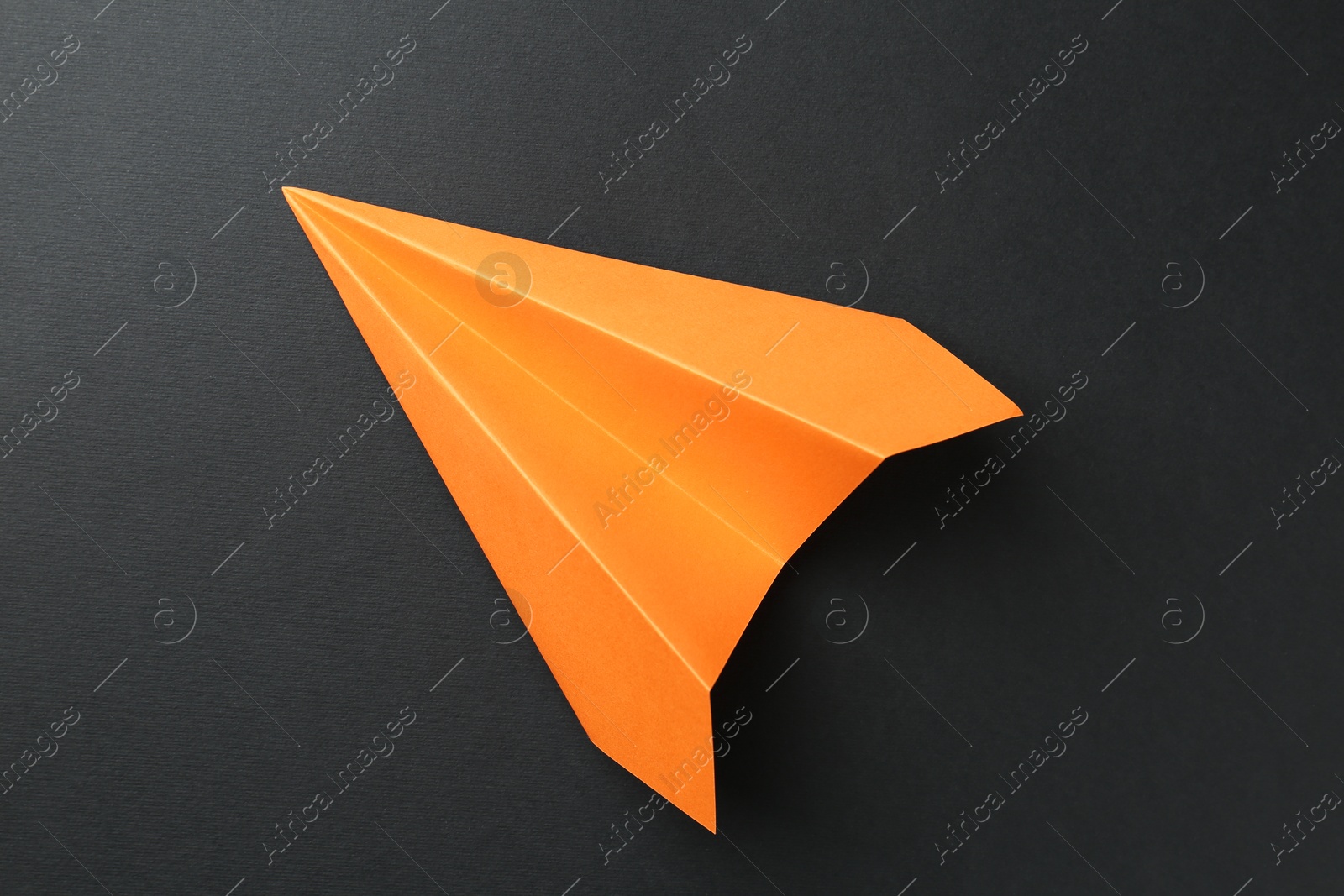 Photo of One handmade orange paper plane on black background, top view