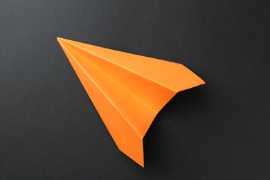 Photo of One handmade orange paper plane on black background, top view