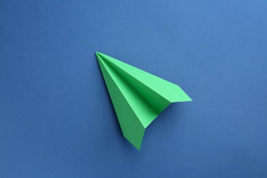 Photo of One handmade green paper plane on blue background, top view