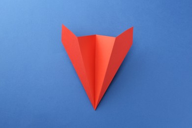 Photo of One handmade coral paper plane on blue background, top view