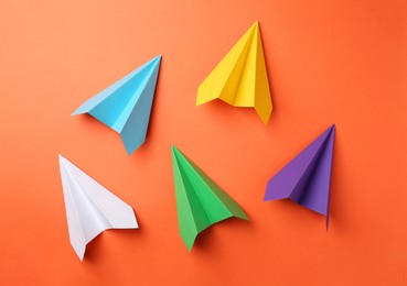 Photo of Handmade color paper planes on orange background, flat lay