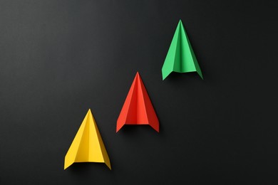 Photo of Handmade color paper planes on black background, flat lay