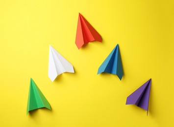 Photo of Handmade color paper planes on yellow background, flat lay