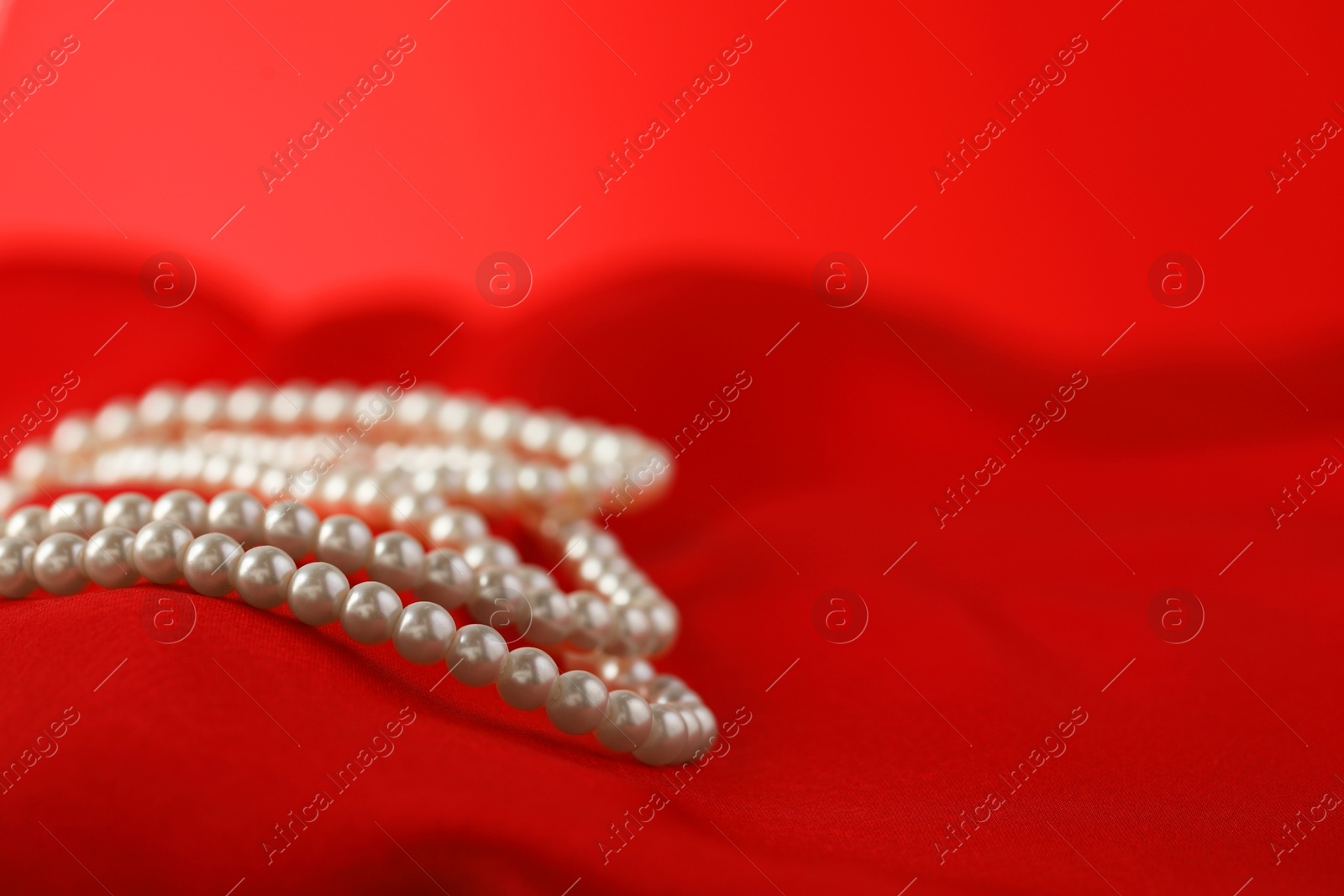 Photo of Beautiful pearl necklace on red silk, closeup. Space for text