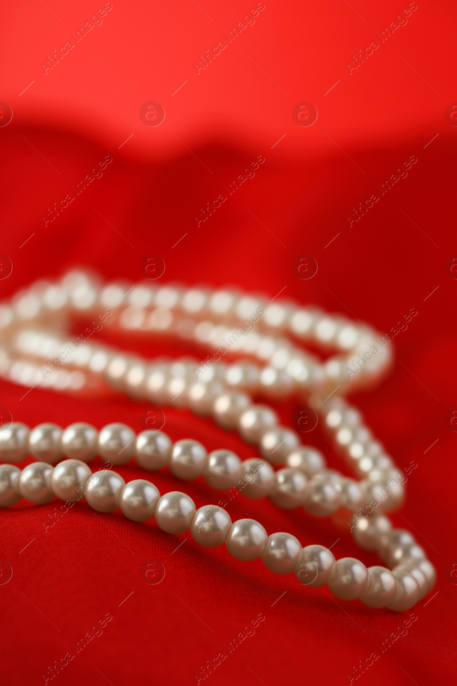 Photo of Beautiful pearl necklace on red silk, closeup