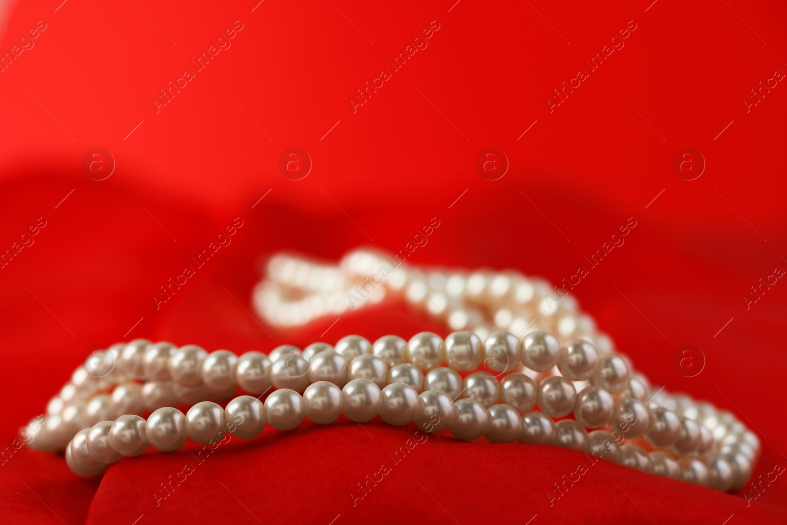 Photo of Beautiful pearl necklace on red silk, closeup