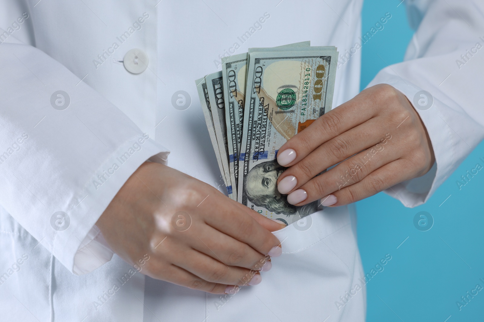 Photo of Corruption concept. Doctor putting dollar banknotes into her pocket on light blue background, closeup