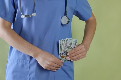 Photo of Corruption concept. Doctor putting dollar banknotes into her pocket on green background, closeup