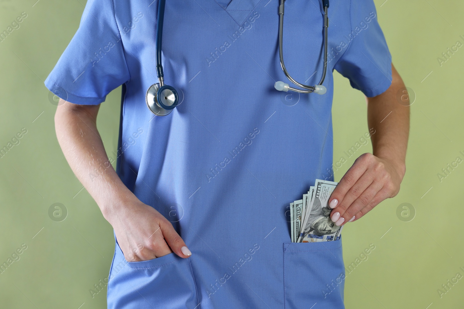 Photo of Corruption concept. Doctor putting dollar banknotes into her pocket on green background, closeup