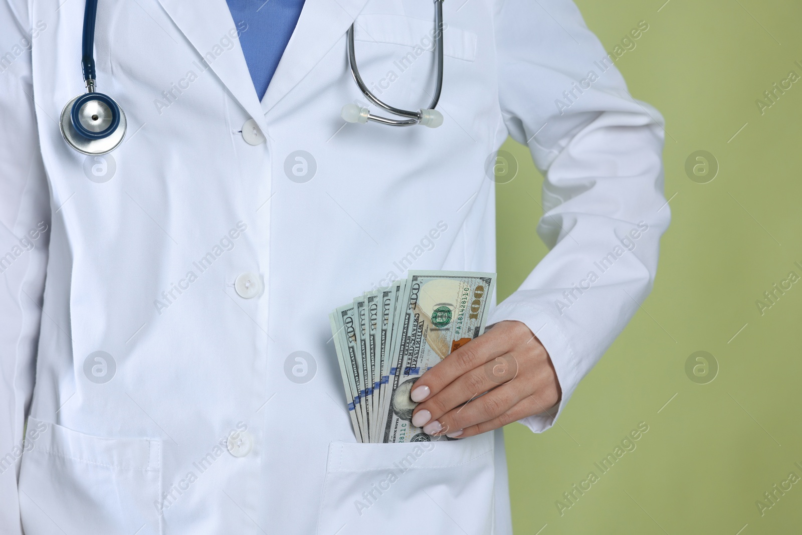 Photo of Corruption concept. Doctor putting dollar banknotes into her pocket on green background, closeup