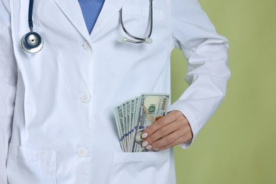 Photo of Corruption concept. Doctor putting dollar banknotes into her pocket on green background, closeup