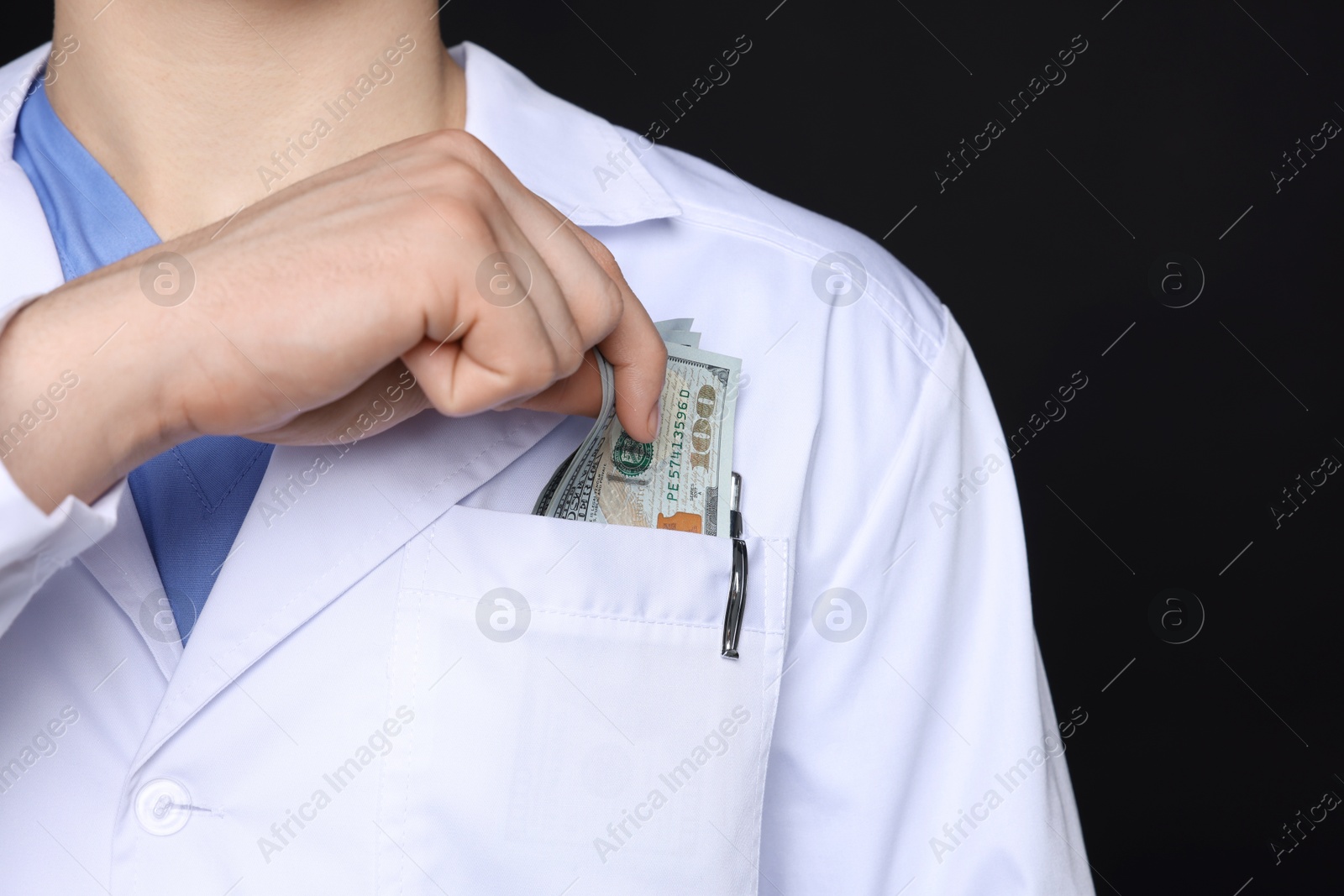 Photo of Corruption concept. Doctor putting dollar banknotes into his pocket on black background, closeup