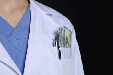 Photo of Corruption concept. Doctor with dollar banknotes in his pocket on black background, closeup