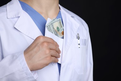 Photo of Corruption concept. Doctor hiding envelope with dollar banknotes on black background, closeup