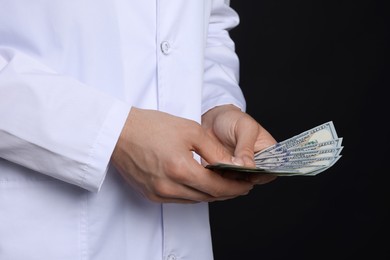 Photo of Corruption concept. Doctor with dollar banknotes on black background, closeup