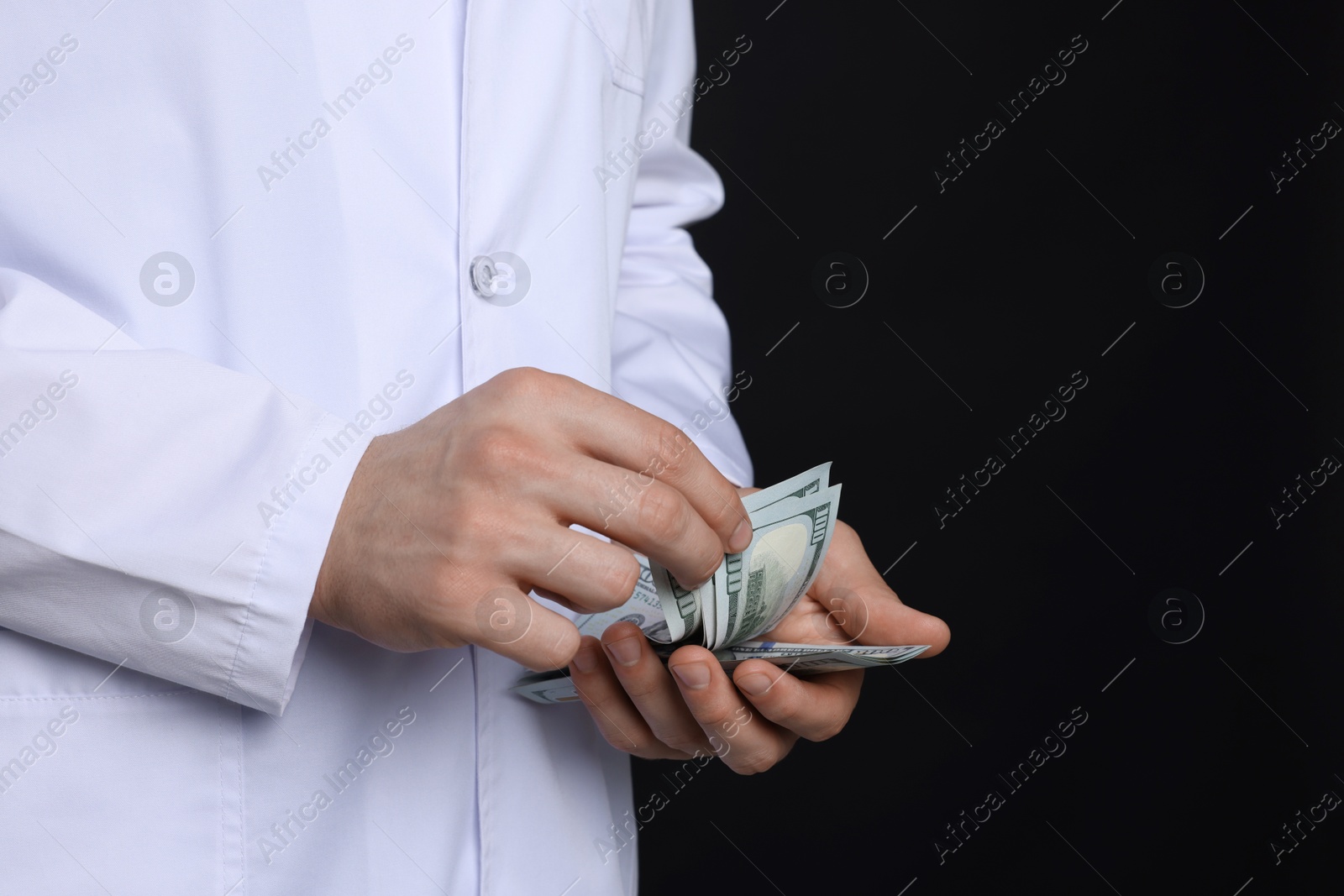 Photo of Corruption concept. Doctor with dollar banknotes on black background, closeup