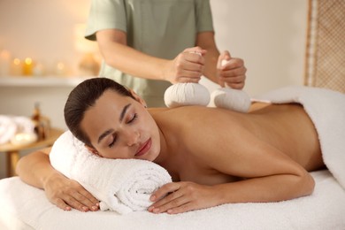 Photo of Woman receiving back massage with herbal bags in spa salon