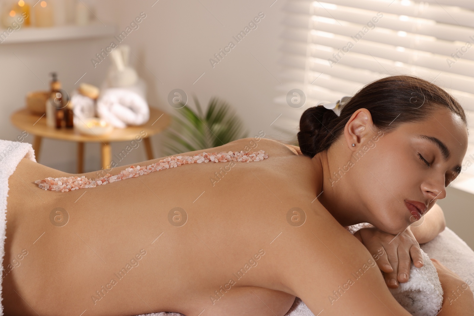 Photo of Woman with sea salt on her back lying on massage table in spa salon