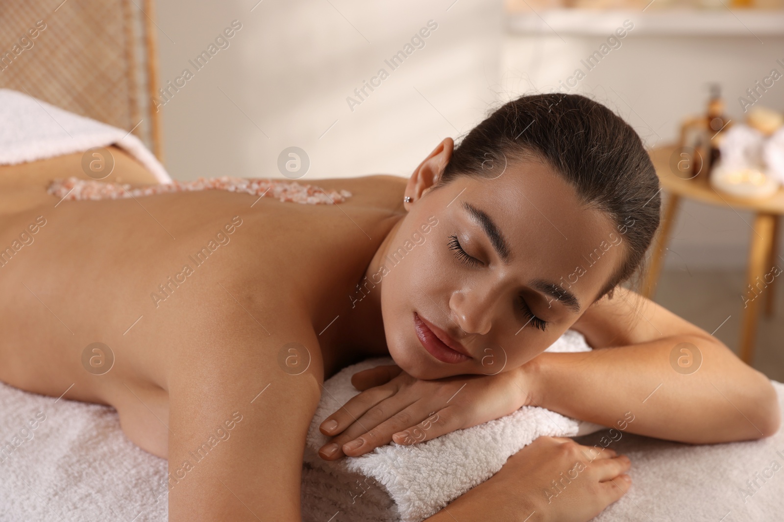 Photo of Woman with sea salt on her back lying on massage table in spa salon