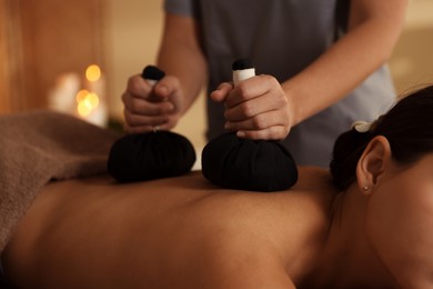 Photo of Woman receiving back massage with herbal bags in spa salon, closeup