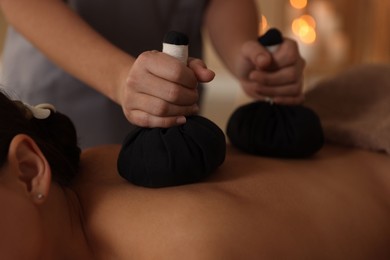 Photo of Woman receiving back massage with herbal bags in spa salon, closeup