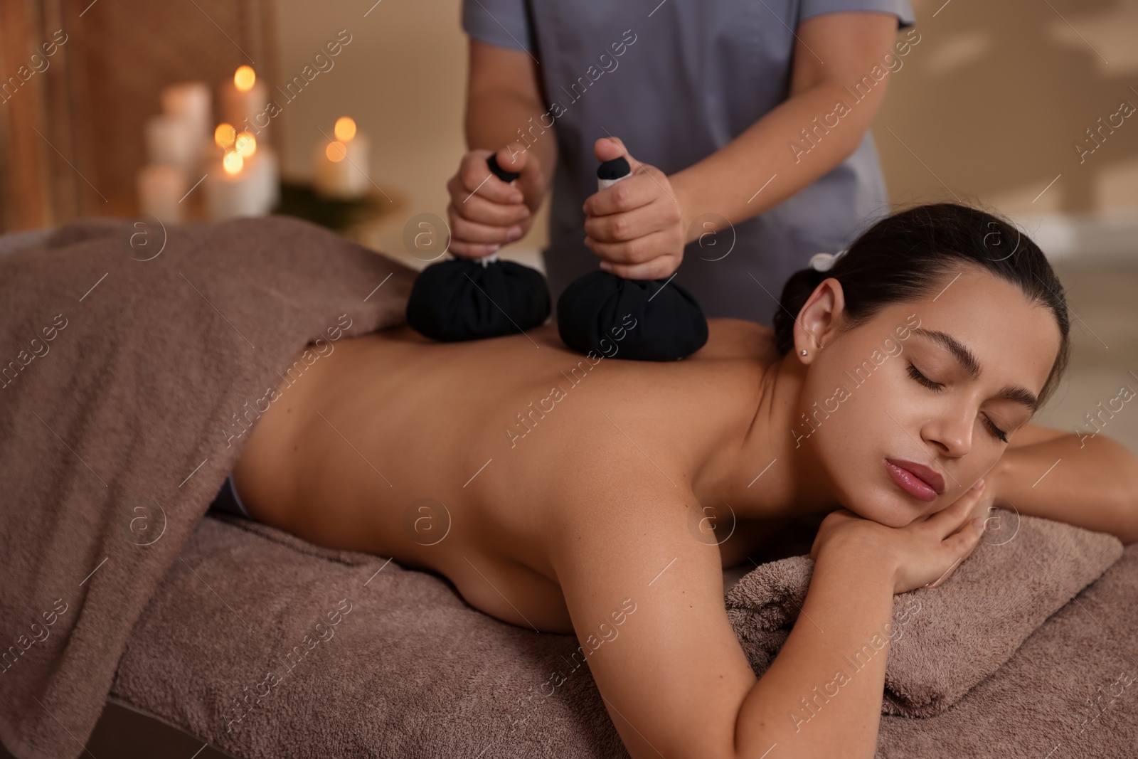 Photo of Woman receiving back massage with herbal bags in spa salon