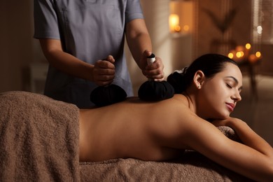 Woman receiving back massage with herbal bags in spa salon