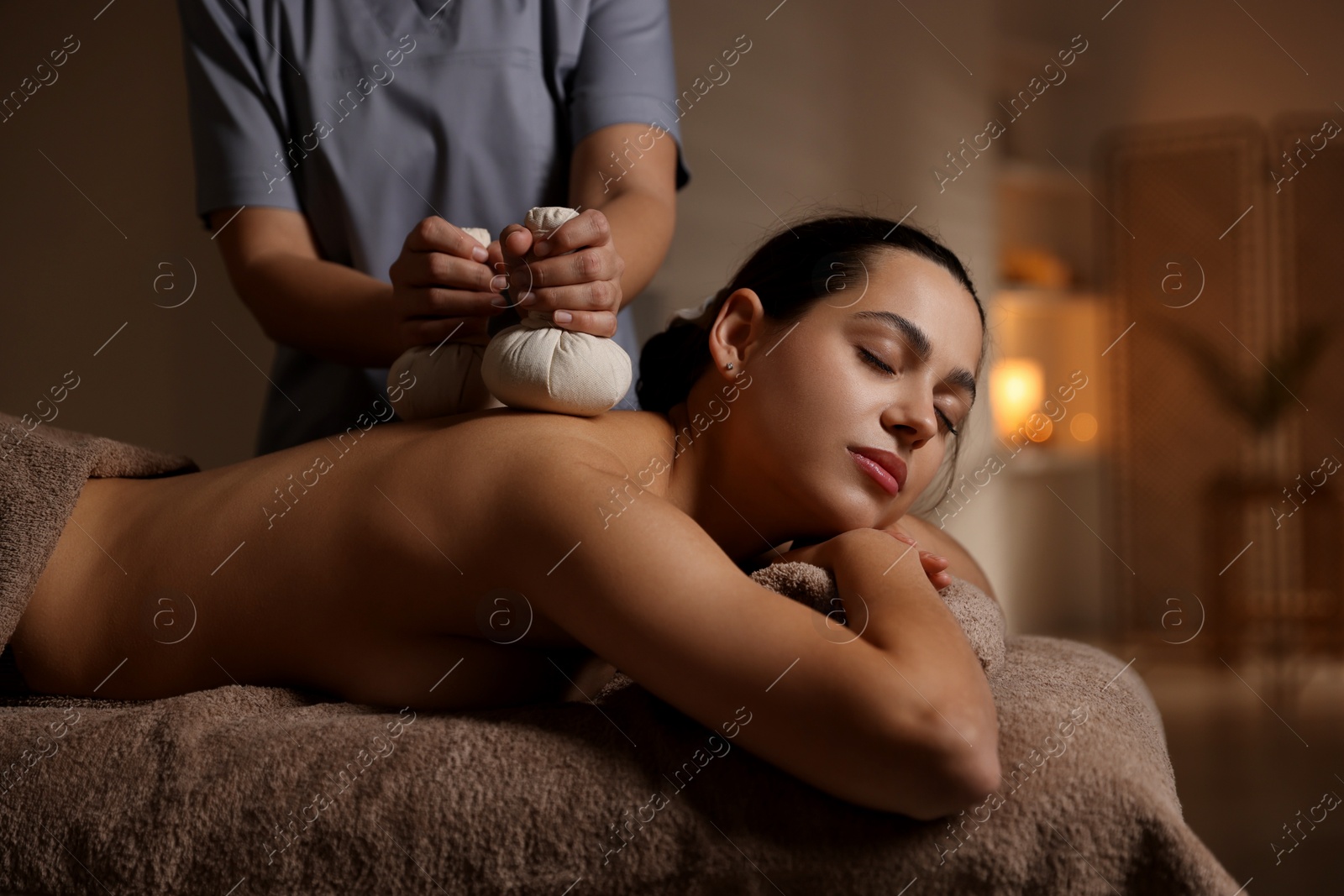 Photo of Woman receiving back massage with herbal bags in spa salon