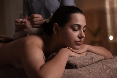 Woman receiving back massage with herbal bags in spa salon