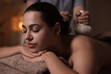 Photo of Woman receiving back massage with herbal bags in spa salon