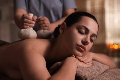 Photo of Woman receiving back massage with herbal bags in spa salon