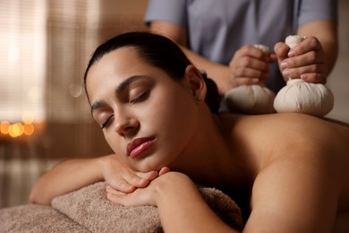 Photo of Woman receiving back massage with herbal bags in spa salon