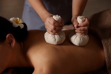 Woman receiving back massage with herbal bags in spa salon, closeup