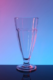 Photo of One empty glass on table against color background