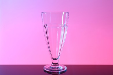 Photo of One empty glass on table against color background