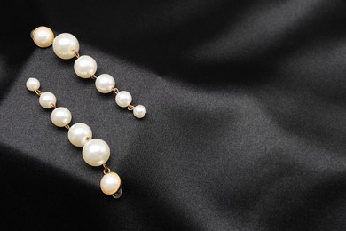 Photo of Beautiful pearl earrings on black cloth, top view. Space for text