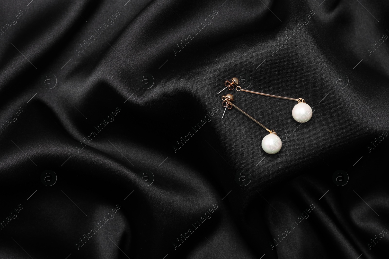 Photo of Beautiful pearl earrings on black cloth, top view. Space for text