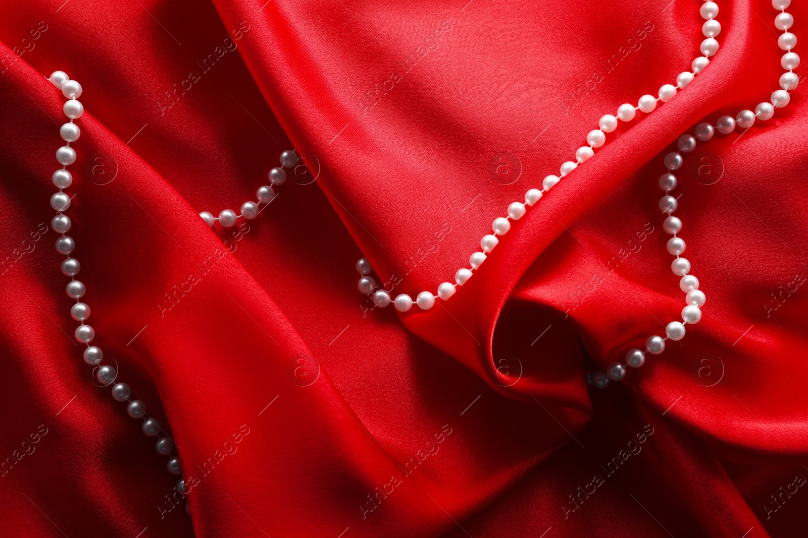 Photo of Beautiful pearl necklace on red cloth, top view