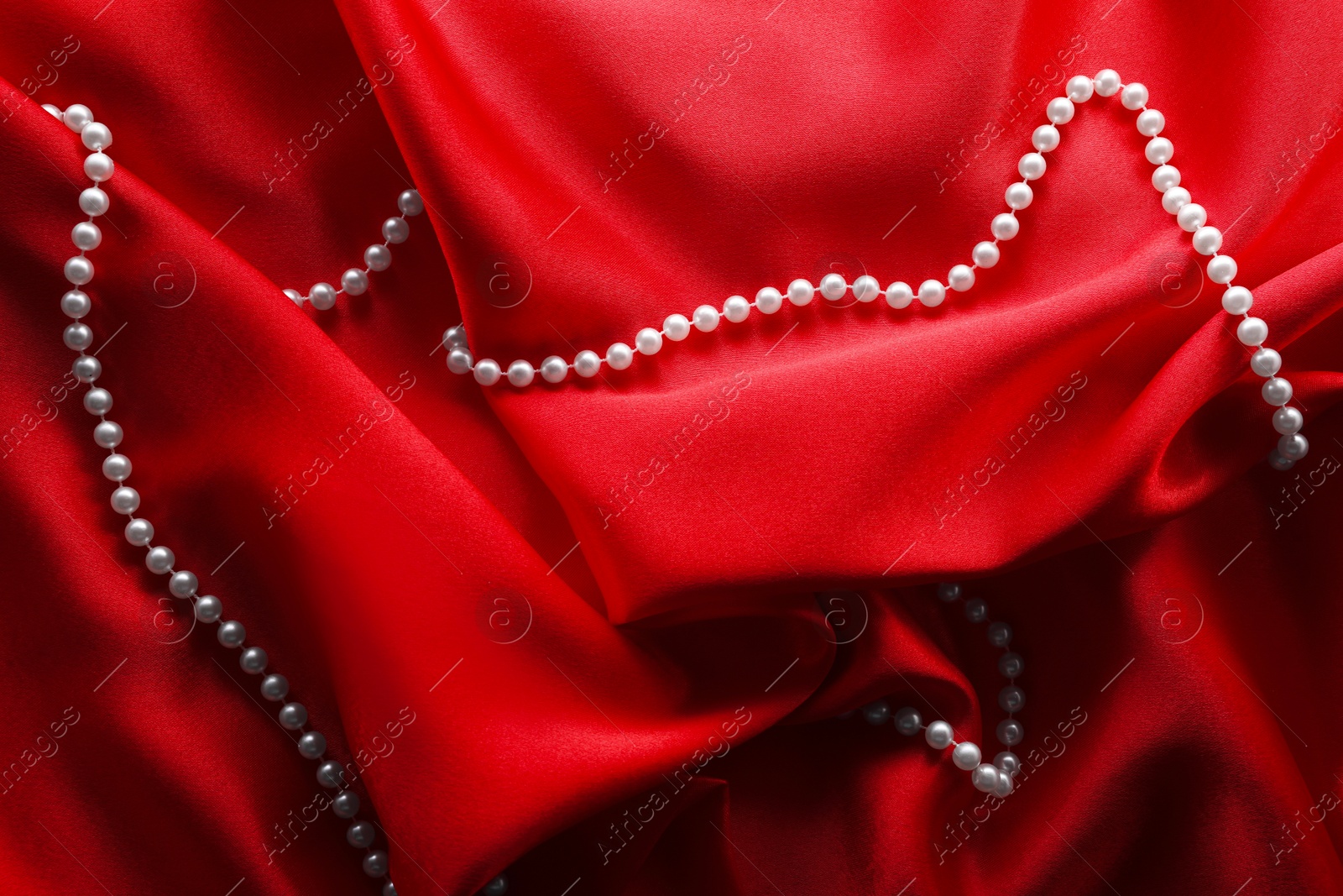 Photo of Beautiful pearl necklace on red cloth, top view