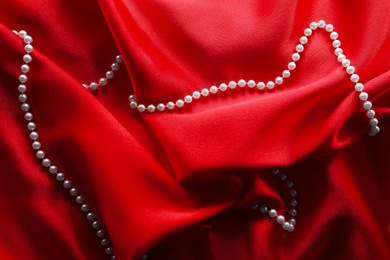 Photo of Beautiful pearl necklace on red cloth, top view