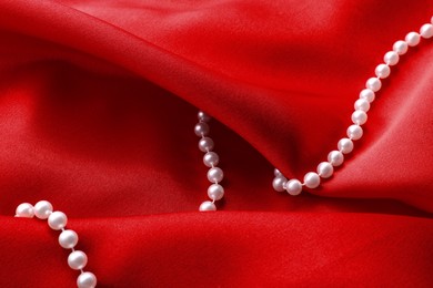 Photo of Beautiful pearl necklace on red cloth, top view