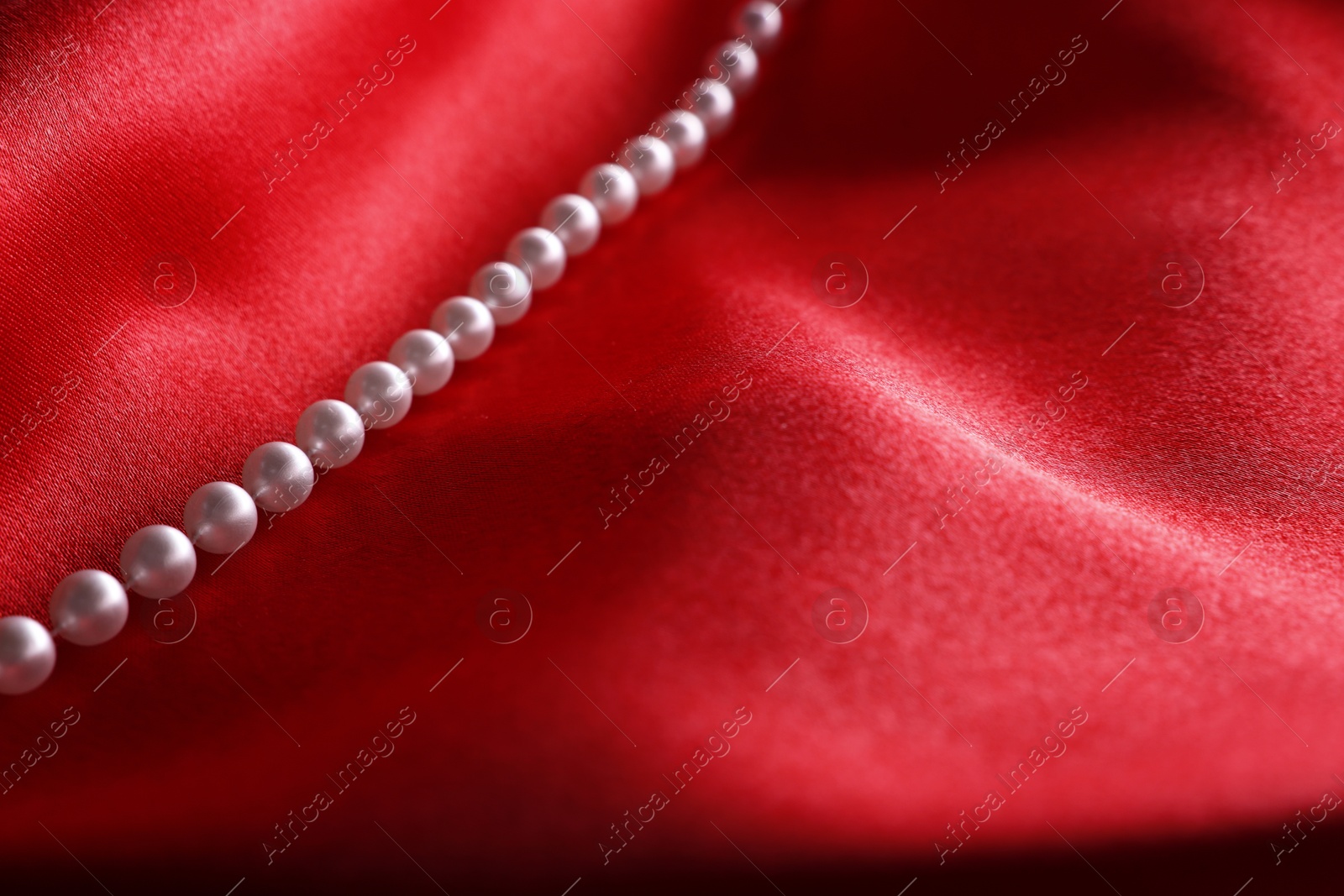 Photo of Beautiful pearl necklace on red cloth, closeup. Space for text